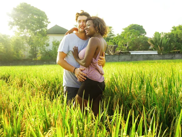 Jong gelukkig en mooi gemengd etnisch paar met zwarte Afro-Amerikaanse vrouw en aantrekkelijke blanke man knuffelen en genieten van vakantie op rijstveld — Stockfoto