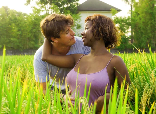 happy and beautiful mixed ethnicity couple with black afro American woman and attractive Caucasian man cuddling and having fun enjoying holidays at rice field