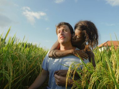 Genç, mutlu ve güzel etnik kökenli çift siyah Afrikalı Amerikalı kadın ve çekici beyaz erkek pirinç tarlasında sarılıp eğleniyorlar.