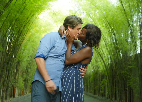 Gelukkig gemengd etniciteit paar zoenen buitenshuis met aantrekkelijke zwarte Afro-Amerikaanse vrouw en knappe Kaukasische vriendje of man in romantische bomen bg — Stockfoto