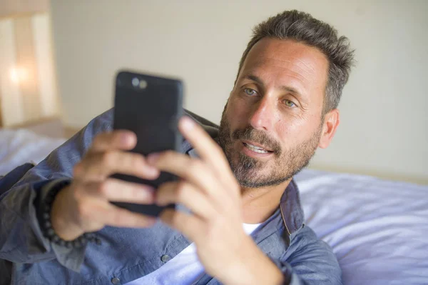 Joven guapo y feliz hombre en casa utilizando el teléfono móvil de Internet en la cama sonriendo alegre y satisfecho sensación relajado citas en línea o disfrutar de las redes sociales aplicación — Foto de Stock