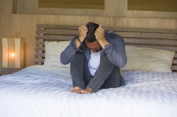 Jovem oprimido e deprimido homem sentado na cama preocupado e frustrado sofrendo crise de depressão puxando o cabelo se sentindo desesperado e indefeso — Fotografia de Stock
