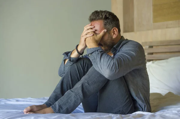 Jovem atraente oprimido e deprimido homem sentado na cama preocupado e frustrado sofrendo crise de depressão cobrindo rosto com as mãos se sentindo desesperado — Fotografia de Stock