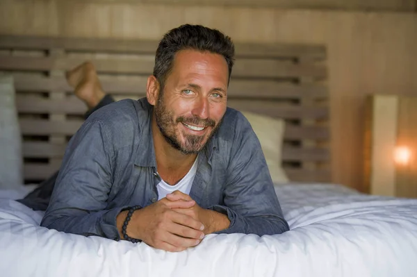 30s hombre feliz y guapo en casa en camisa casual y jeans acostado en la cama relajado en casa sonriendo confiado y feliz sentirse positivo en el concepto de estilo de vida masculino — Foto de Stock