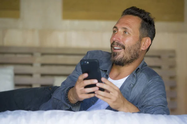 Joven guapo y feliz hombre en casa utilizando el teléfono móvil de Internet en la cama sonriendo alegre y satisfecho sensación relajado citas en línea o disfrutar de las redes sociales aplicación — Foto de Stock