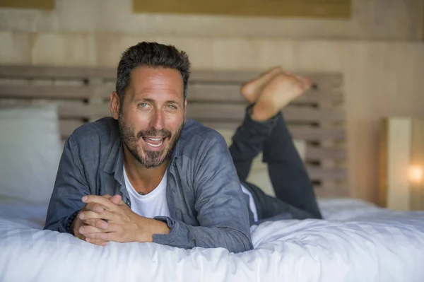 30s hombre feliz y guapo en casa en camisa casual y jeans acostado en la cama relajado en casa sonriendo confiado y feliz sentirse positivo en el concepto de estilo de vida masculino — Foto de Stock