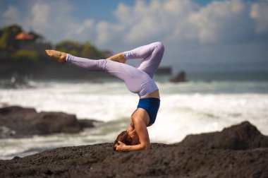 young attractive and concentrated woman practicing acroyoga balance exercise and yoga flexibility and meditation on the sea at beautiful tropical beach rock