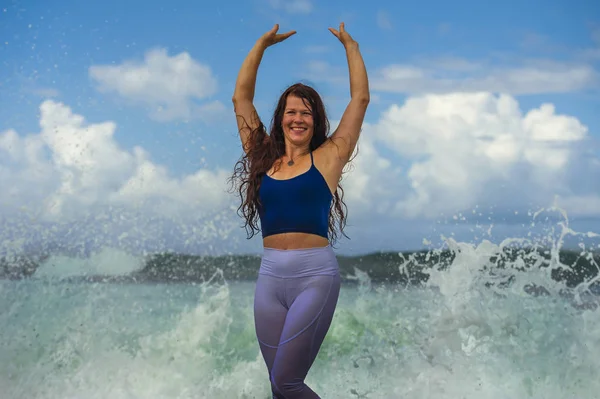 Young happy and attractive red hair woman playing excited spreading arms feeling free and relaxed getting wet by sea waves splashing on her enjoying beach — Stock Photo, Image