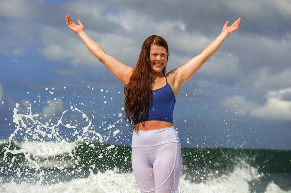 Joven feliz y atractiva mujer pelirroja jugando brazos extendidos emocionados sintiéndose libre y relajado mojándose por las olas del mar salpicando en su playa disfrutando — Foto de Stock