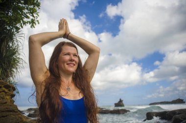 genç çekici ve mutlu kızıl saçlı kadının doğal portresi meditasyon ve gevşeme yoga lotus egzersiz pratik deniz arka planda plaj kaya oturan