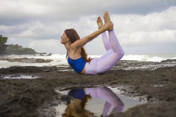 Młody szczęśliwy atrakcyjne i piękne rude włosy kobieta praktykujących jogi medytacji i ćwiczenia elastyczności na plaży na skałach w pięknym tle morza — Zdjęcie stockowe