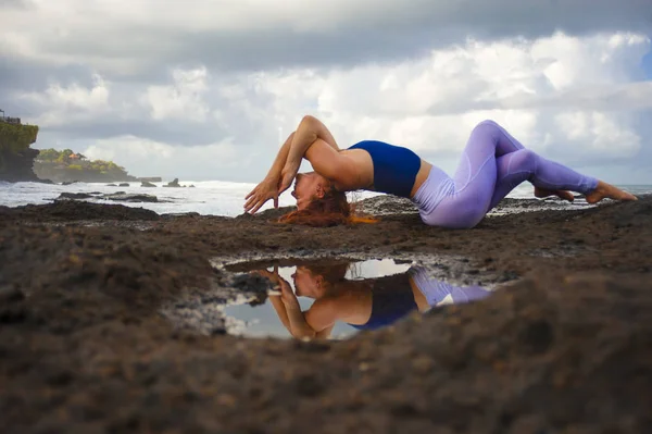 Молодые счастливые привлекательные и красивые рыжие волосы женщина практикует йогу медитации и гибкость упражнения на пляже на скалах в красивом морском фоне — стоковое фото