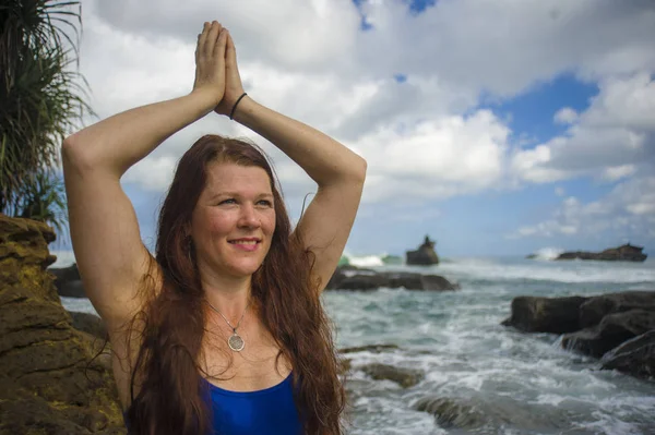 Natural portrait of young attractive and happy red hair woman practicing meditation and relaxation yoga lotus exercise sitting at beach rock on the sea background — Stock Photo, Image