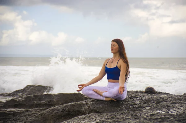 Natural portrait of young attractive and happy red hair woman practicing meditation and relaxation yoga lotus exercise sitting at beach rock on the sea background — Stock Photo, Image