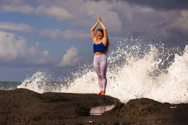 Естественный портрет молодой красивой и счастливой женщины с рыжими волосами, практикующей медитацию и релаксацию йоги лотоса, стоящей у береговой скалы на берегу моря — стоковое фото