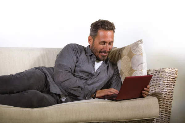 Портрет природного способу життя молодого красивого і успішного працевлаштованого чоловіка, який працює вдома, використовуючи ноутбук, що лежить розслаблений на живих диванних мережах — стокове фото