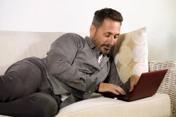 Портрет природного способу життя молодого красивого і успішного працевлаштованого чоловіка, який працює вдома, використовуючи ноутбук, що лежить розслаблений на живих диванних мережах — стокове фото
