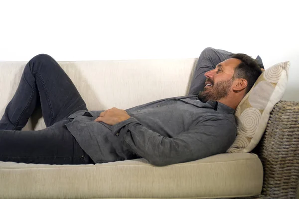 lifestyle home portrait of young attractive and happy white man with beard and casual shirt lying relaxed and cozy at living room sofa couch resting and smiling cheerful