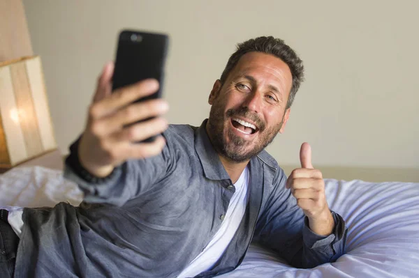 Stile di vita ritratto di giovane attraente e felice anni 30 o 40 uomo scattare foto selfie con il telefono cellulare sorridente gesti giocosi a casa camera da letto sdraiato sul letto — Foto Stock
