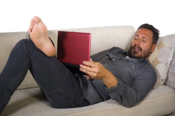 natural lifestyle portrait of young handsome and successful self employed man working at home using laptop computer lying relaxed at living couch networking