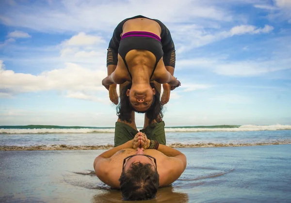 Young attractive and concentrated couple of acrobats practicing acro yoga balance and meditation exercise on beautiful beach under a blue sky in mind and body control — Stock Photo, Image