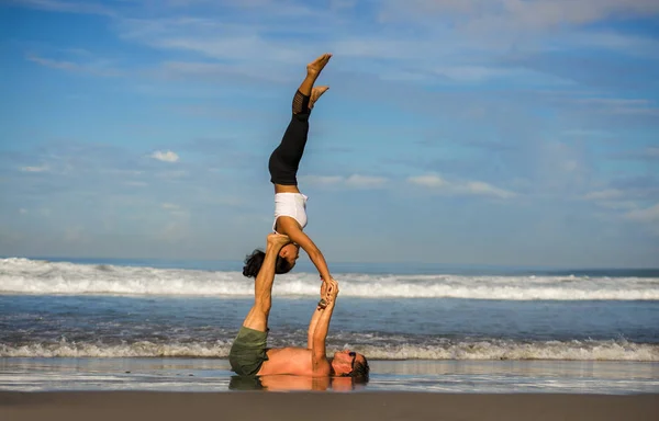 Outdoors lifestyle portrait young attractive and concentrated couple of yoga acrobats practicing acroyoga balance and meditation exercise on beautiful beach — Stock Photo, Image