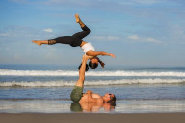 Genç çekici ve konsantre olmuş bir çift akro yoga dengesi ve meditasyon egzersizi yapan akrobat. Mavi bir gökyüzü altında zihin ve beden kontrolü.