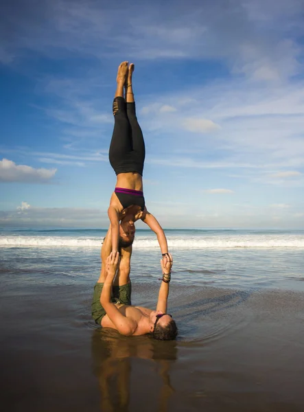 outdoors lifestyle portrait young attractive and concentrated couple of yoga acrobats practicing acroyoga balance and meditation exercise on beautiful beach