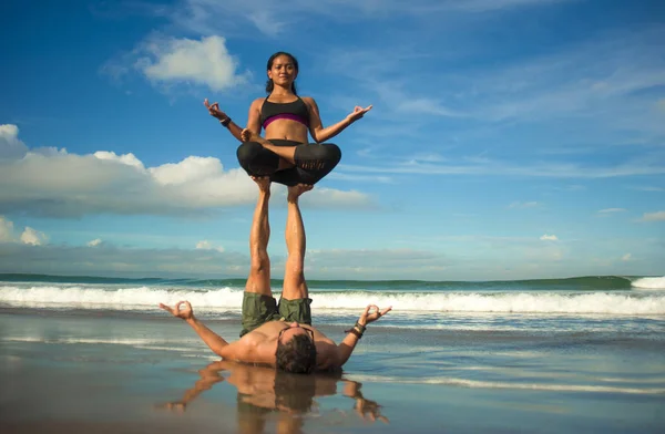 Outdoors lifestyle portrait young attractive and concentrated couple of yoga acrobats practicing acroyoga balance and meditation exercise on beautiful beach — Stock Photo, Image