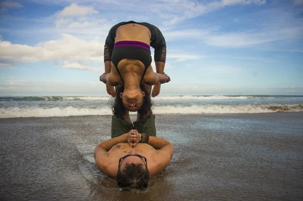 Outdoors lifestyle portrait young attractive and concentrated couple of yoga acrobats practicing acroyoga balance and meditation exercise on beautiful beach — Stock Photo, Image