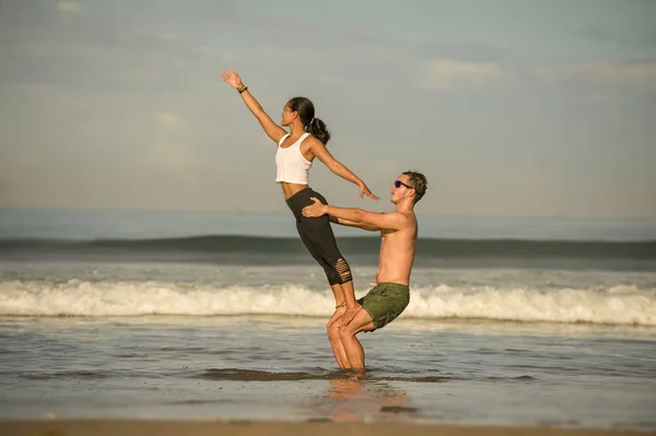 young attractive and concentrated couple of acrobats practicing acro yoga balance and meditation exercise on beautiful beach under a blue sky in mind and body control