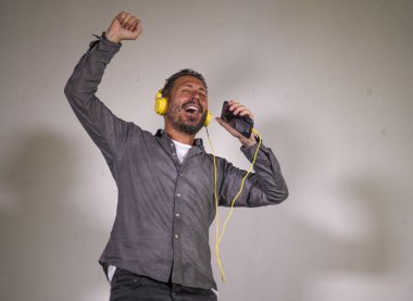 40s mutlu ve heyecanlı çekici adam kulaklık ve cep telefonu şarkı şarkı ve stüdyo arka plan izole kaygısız dans ile online müzik dinlerken