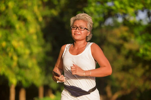 Mujer feliz y atractiva de 40 o 50 años de edad con entrenamiento de pelo gris en el parque de la ciudad con árboles verdes al amanecer haciendo ejercicio de correr y correr en el cuidado de la salud — Foto de Stock