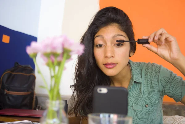 Estilo de vida retrato de joven hermosa y atractiva morena latina retocando pestañas maquillaje de rímel usando el teléfono móvil como espejo sentado en la cafetería — Foto de Stock