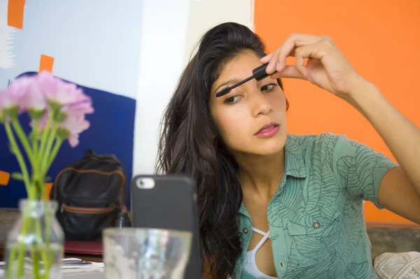Estilo de vida retrato de joven hermosa y atractiva morena latina retocando pestañas maquillaje de rímel usando el teléfono móvil como espejo sentado en la cafetería — Foto de Stock
