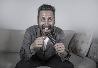 Genç, çekici ve mutlu bir adam evinde gülüyor televizyon programı ya da komedi dizisi seyrediyor oturma odasındaki koltukta rahat ve neşeli oturuyor.