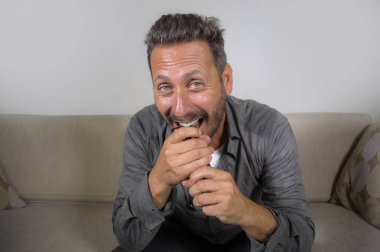 Genç, çekici ve mutlu bir adam evinde gülüyor televizyon programı ya da komedi dizisi seyrediyor oturma odasındaki koltukta rahat ve neşeli oturuyor.