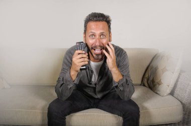 30'larında ya da 40'lı yaşlarında heyecanlı ve çekici bir adam evde spor maçı veya gerilim filmi izlerken eğleniyor televizyon oturma odasında ki kanepede otururken gergin hissediyorum