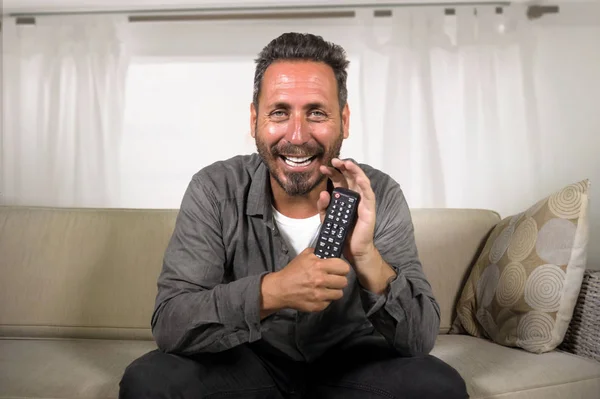 Guapo y feliz hombre blanco de 30 o 40 años viendo hilarante programa de televisión en casa riendo alegre divertirse sentado relajado y fresco en el sofá de la sala de estar — Foto de Stock