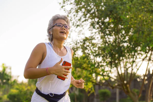 Mujer feliz y atractiva de 40 o 50 años de edad con entrenamiento de pelo gris en el parque de la ciudad con árboles verdes al amanecer haciendo ejercicio de correr y correr en el cuidado de la salud — Foto de Stock