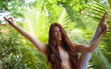 sağlıklı yaşam tarzı inanılmaz tropikal ormanda yoga dengesi egzersiz germe bacak yapıyor güzel uzun kırmızı saçlı genç mutlu ve çekici kadın doğal portre