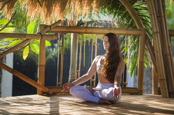 Giovane donna attraente e felice rilassato seduto in posizione loto yoga facendo meditazione e concentrazione all'aperto in capanna di legno nella bella giungla tropicale — Foto Stock