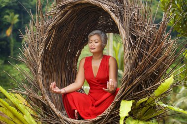 tropik ormanda yoga gevşeme ve meditasyon pratik şık ve güzel kırmızı elbise çekici ve mutlu 40s veya 50s orta yaşlı Asyalı kadın