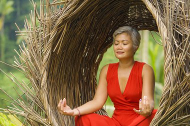 tropik ormanda yoga gevşeme ve meditasyon pratik şık ve güzel kırmızı elbise çekici ve mutlu 40s veya 50s orta yaşlı Asyalı kadın