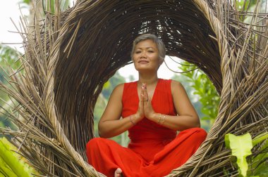 tropik ormanda yoga gevşeme ve meditasyon pratik şık ve güzel kırmızı elbise çekici ve mutlu 40s veya 50s orta yaşlı Asyalı kadın