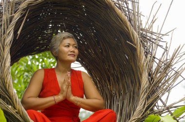 tropik ormanda yoga gevşeme ve meditasyon pratik şık ve güzel kırmızı elbise çekici ve mutlu 40s veya 50s orta yaşlı Asyalı kadın