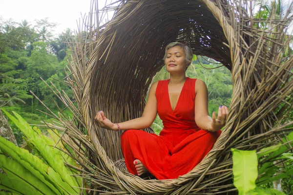 Atractiva y feliz mujer asiática de 40 o 50 años de edad en elegante y hermoso vestido rojo practicando yoga relajación y meditación en la selva tropical — Foto de Stock
