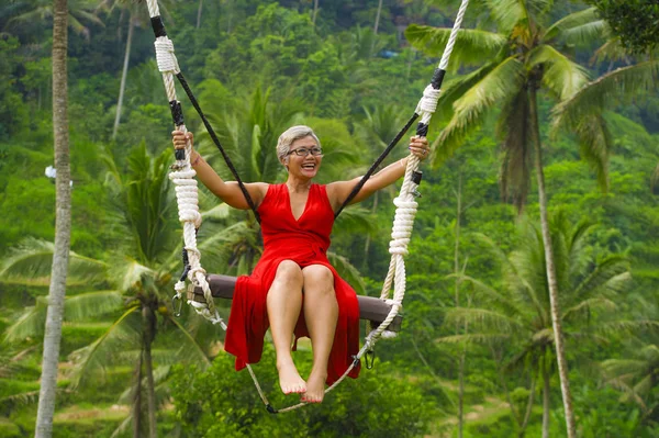 Atractivo feliz de mediana edad de 40 o 50 años mujer indonesia asiática con pelo gris montar selva tropical swing sin preocupaciones balanceo y disfrutar de la aventura de la selva tropical — Foto de Stock