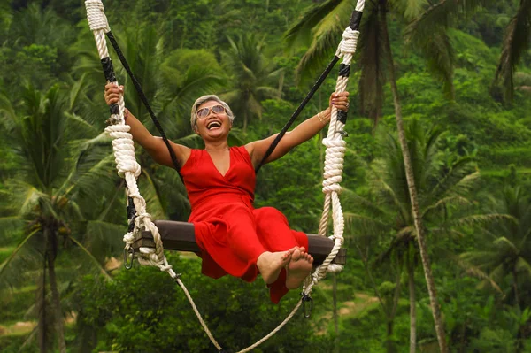Vonzó boldog középkorú 40-es vagy 50-es évek ázsiai indonéz nő, szürke hajú lovaglás esőerdők swing gondtalan lengő és élvezi a trópusi dzsungel kaland — Stock Fotó
