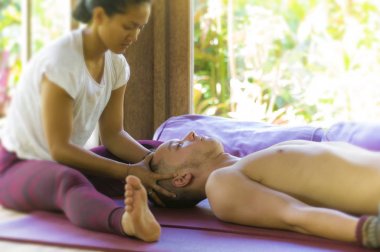 Genç, güzel ve egzotik Asyalı Taylandlı kadın geleneksel baş ve yüz masajı yapıyor. Alternatif tıp spa 'sında beyaz bir adama.